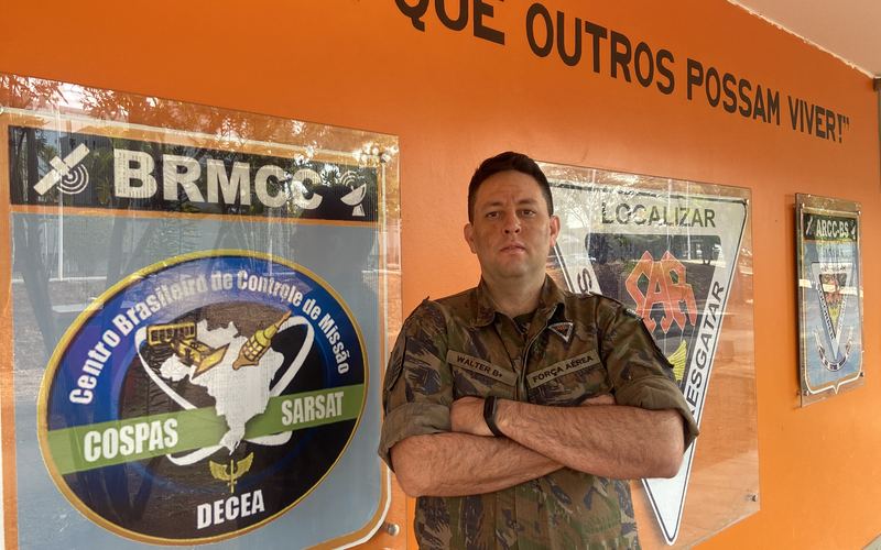 Walter Robôs de farda diante da parede com o lema da busca e salvamento